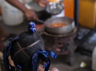 A young girl watches as a woman prepares food in a displacement camp in Haiti